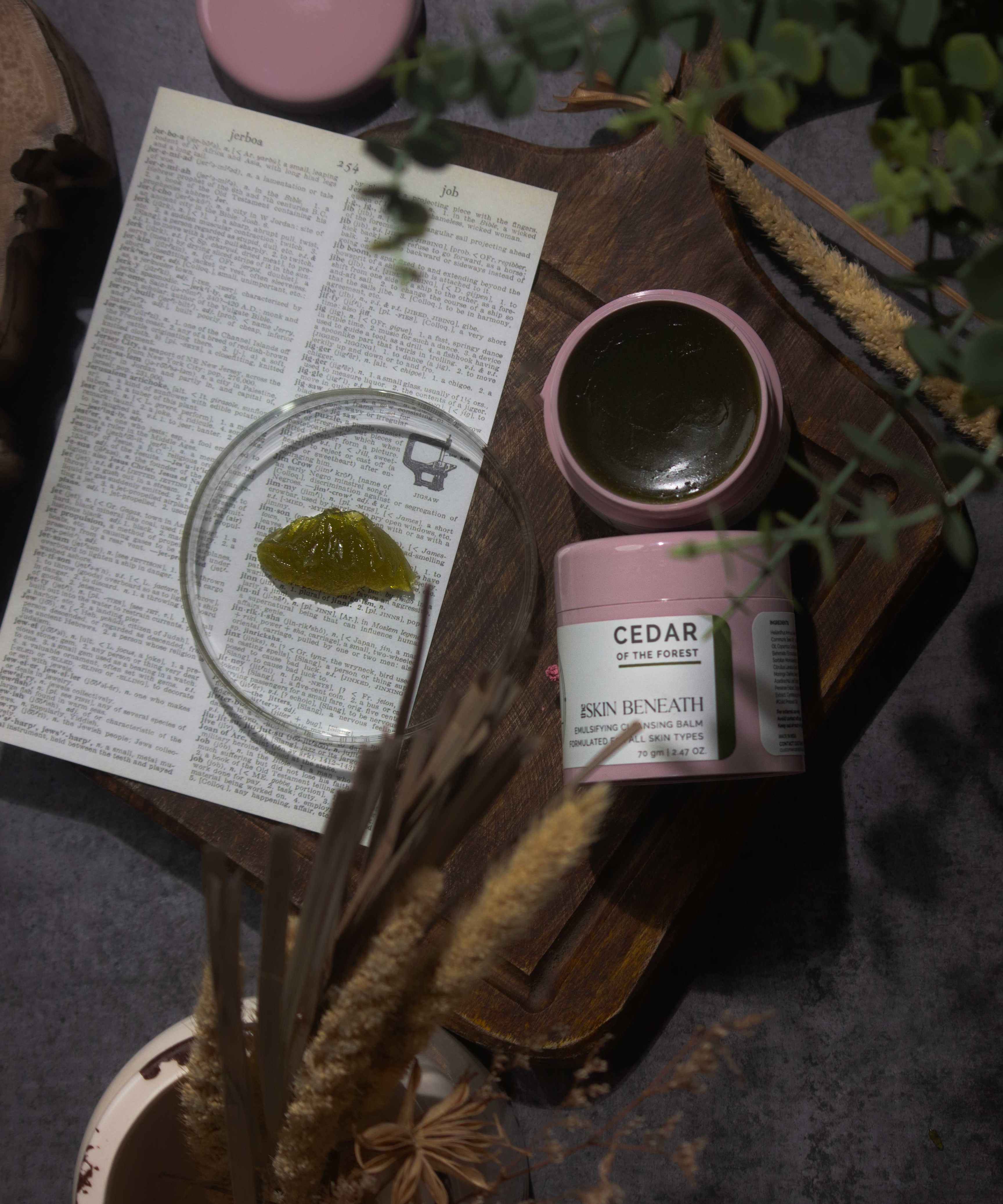 Cedar of the Forest cleansing balm on wooden tray with green, woody elements — forest-inspired flat lay for sensorial skincare ritual