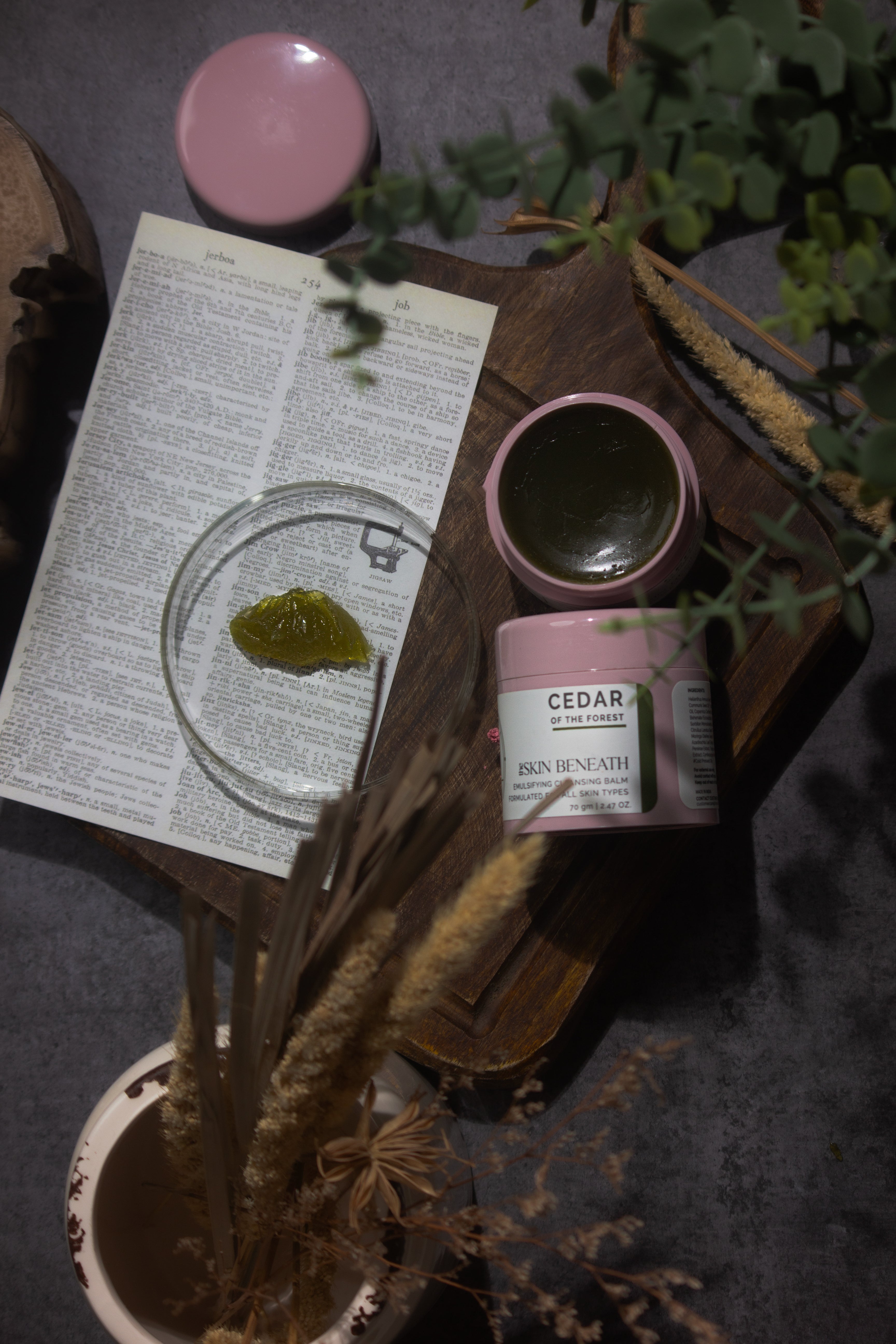 Cedar of the Forest cleansing balm on wooden tray with green, woody elements — forest-inspired flat lay for sensorial skincare ritual