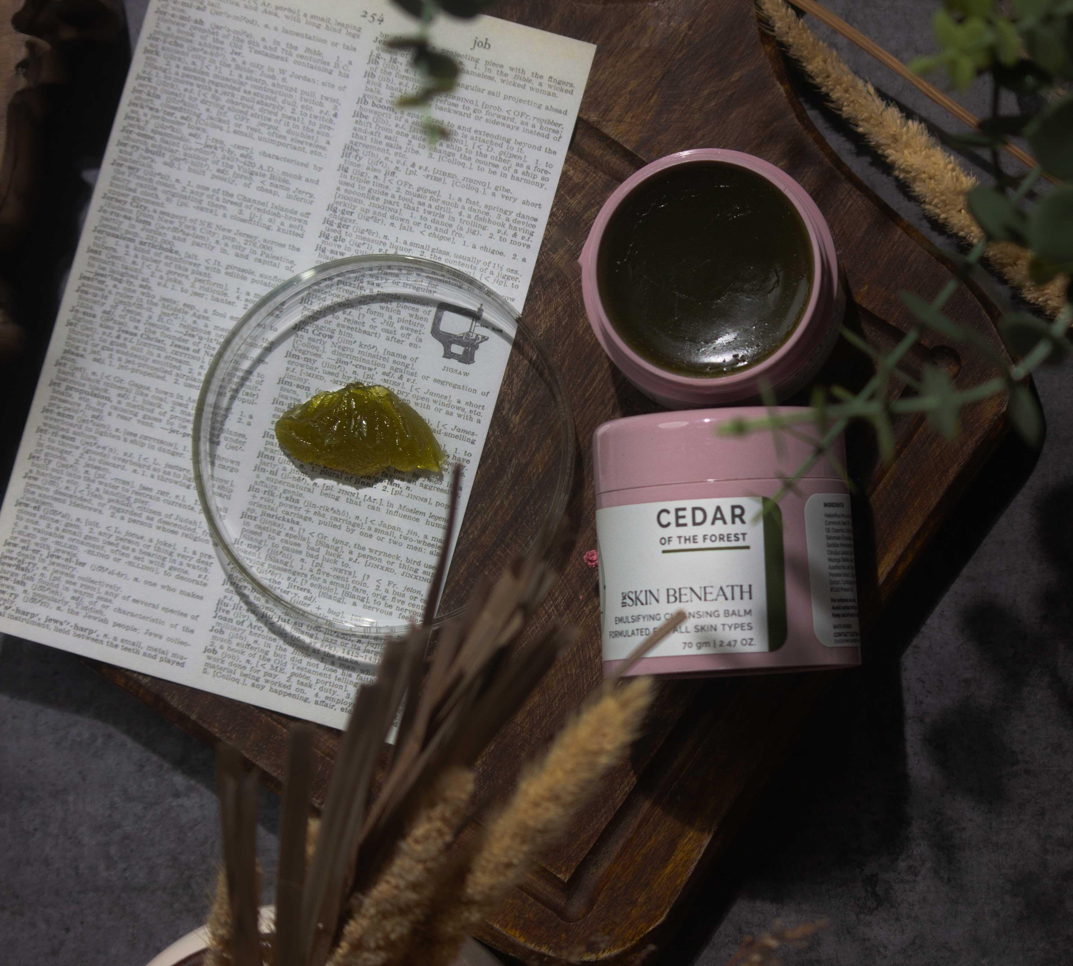Cedar of the Forest cleansing balm on wooden tray with green, woody elements — forest-inspired flat lay for sensorial skincare ritual
