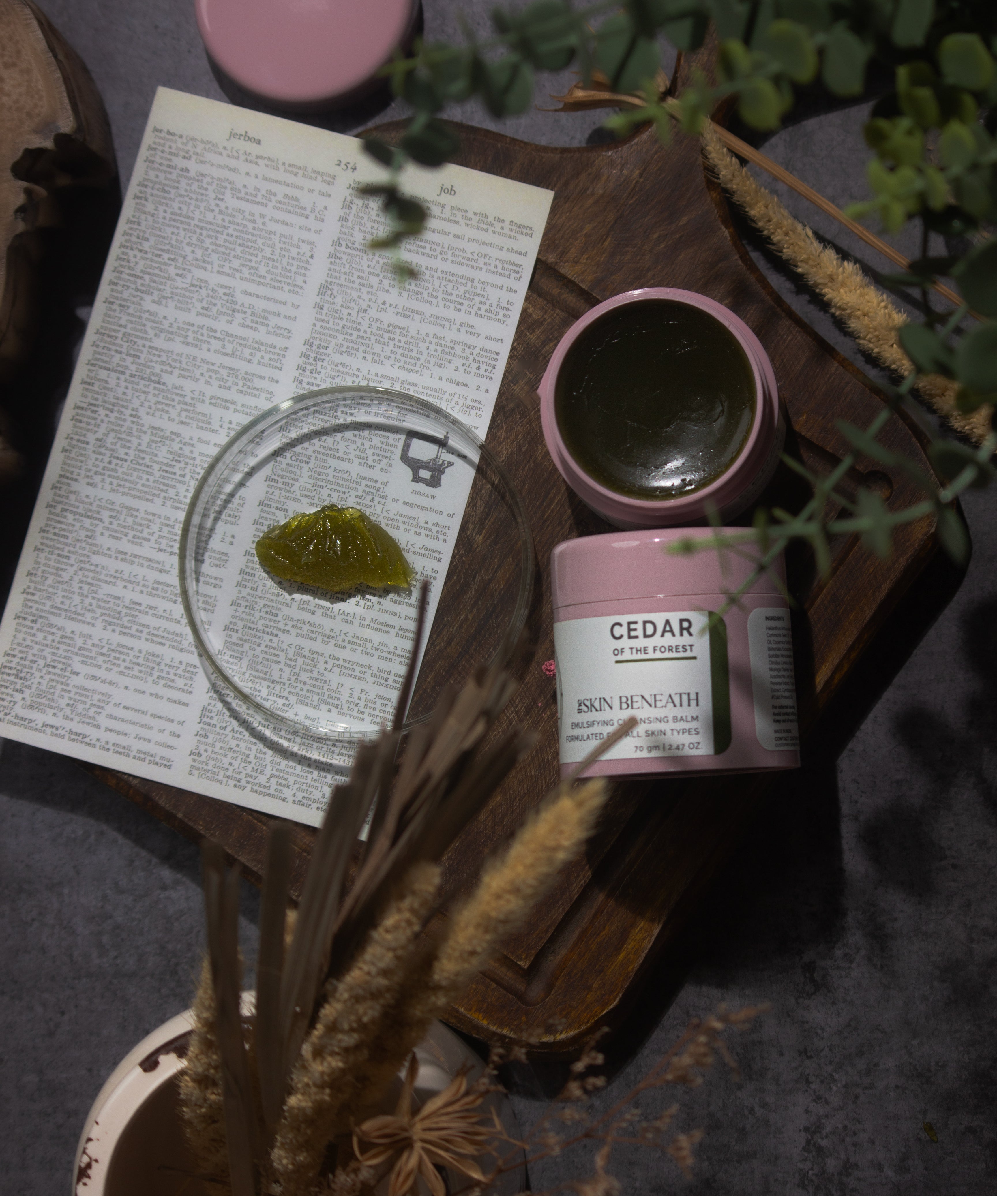 Cedar of the Forest cleansing balm on wooden tray with green, woody elements — forest-inspired flat lay for sensorial skincare ritual