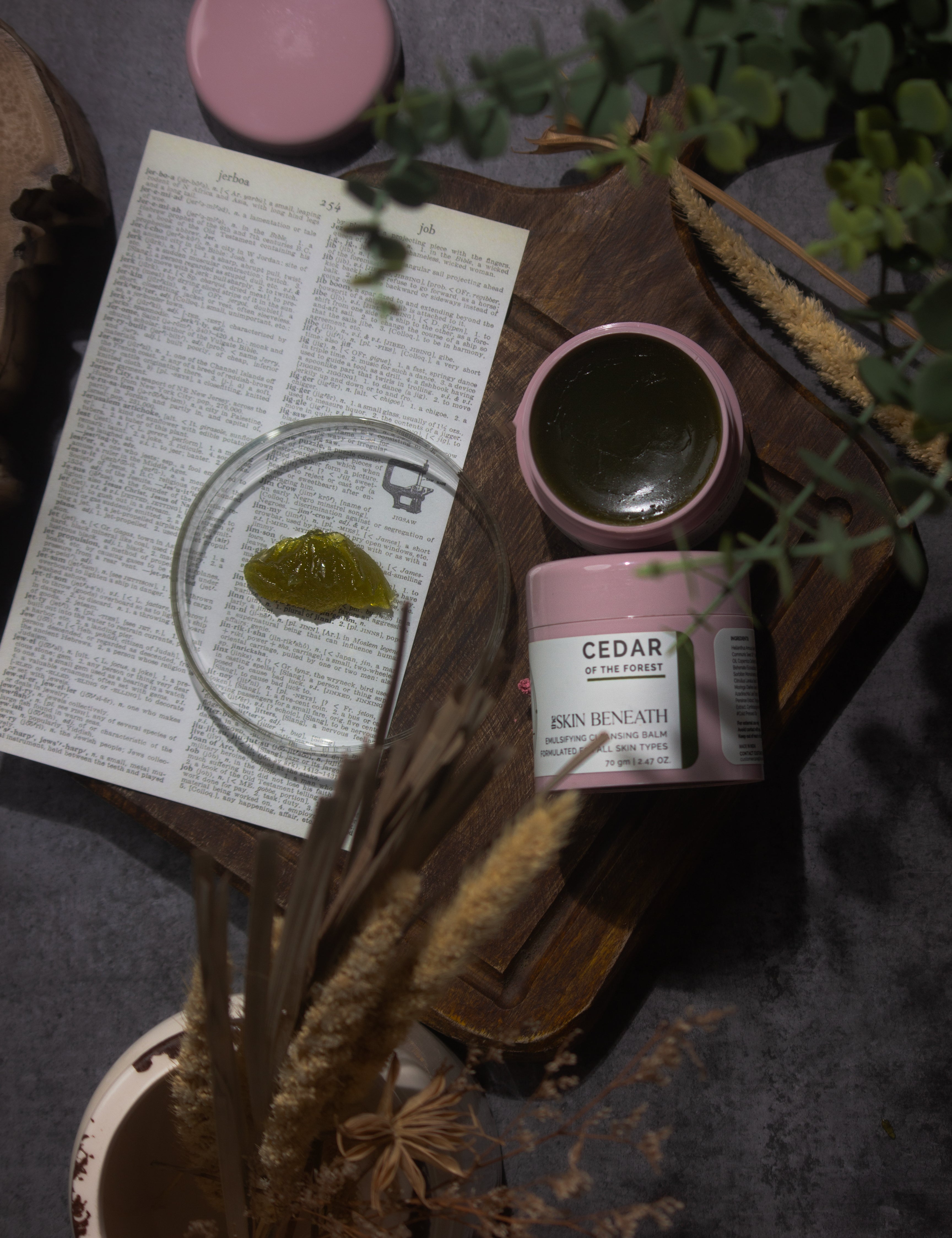 Cedar of the Forest cleansing balm on wooden tray with green, woody elements — forest-inspired flat lay for sensorial skincare ritual
